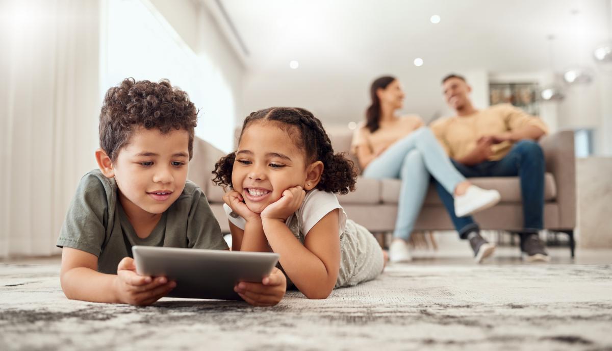 Children enjoying a tablet on the floor while parents relax on the sofa in a bright living room