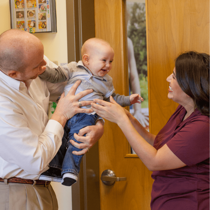 Smiling parents holding a cheerful baby in a cozy room.