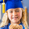 Child smiling in blue graduation cap holding teddy bear