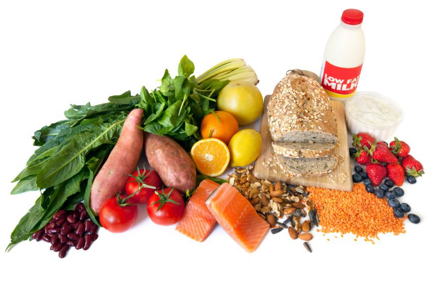 Healthy foods including fruits vegetables bread salmon milk yogurt and nuts arranged on a white background