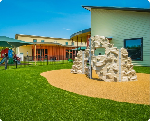 Sunny daycare playground with rock climbing structure and artificial grass next to modern building