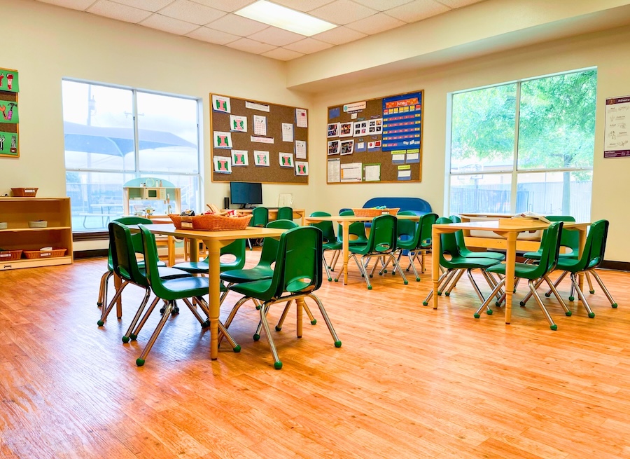 Preschool classroom with small tables chairs and colorful decorations on walls