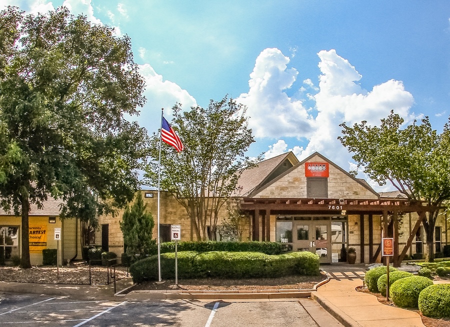 Front view of a childcare center with American flag and trees under a blue sky