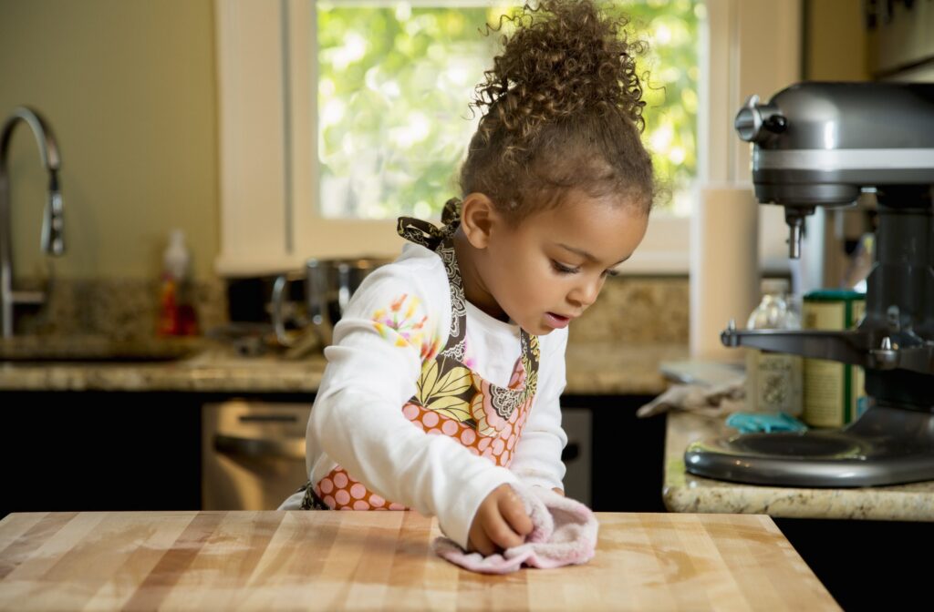 Child cleaning a kitchen counter with a cloth in a sunlit room