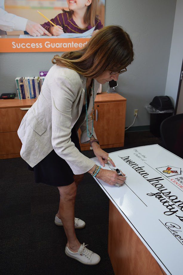 Woman in a blazer signing a large donation check in an office setting