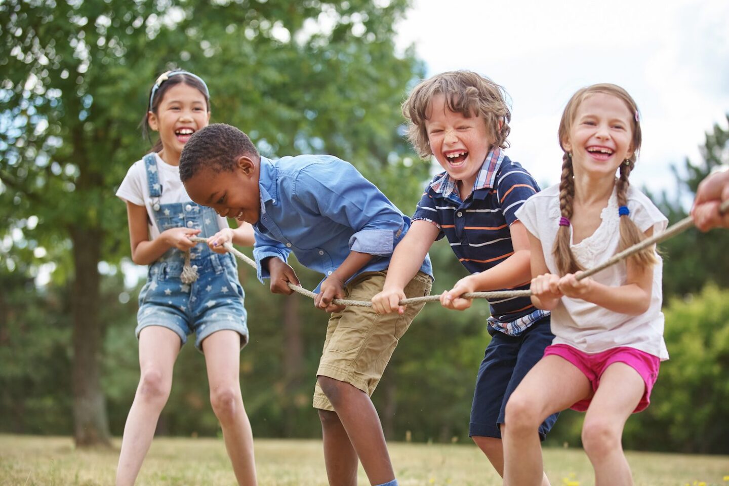 Children playing tug of war and laughing in a sunny park.