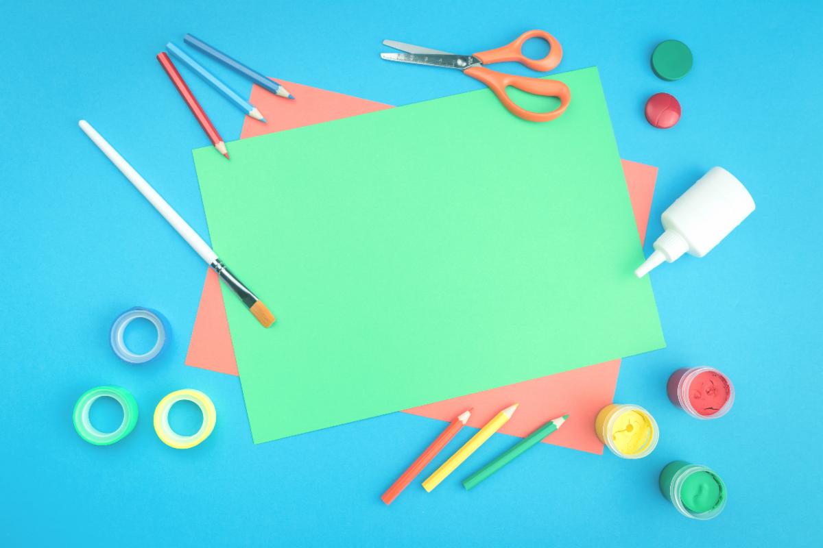 Art supplies on blue background with colored paper pencils paints glue and scissors