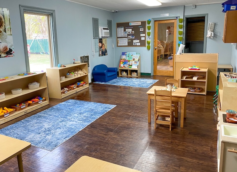 Colorful, organized preschool classroom with toys and activities on shelves and a cozy reading area.