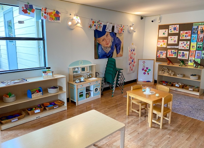 Colorful preschool classroom with art displays and play kitchen set on wooden floor.