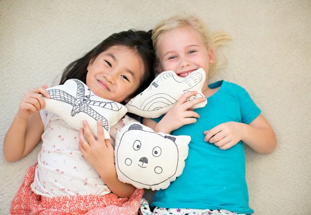 Two children lying on carpet holding animal-themed pillows and smiling