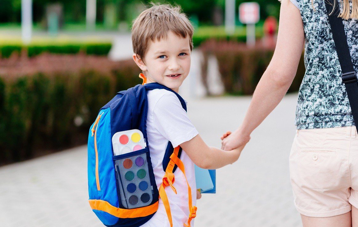 Boy with backpack holding adult's hand outdoors