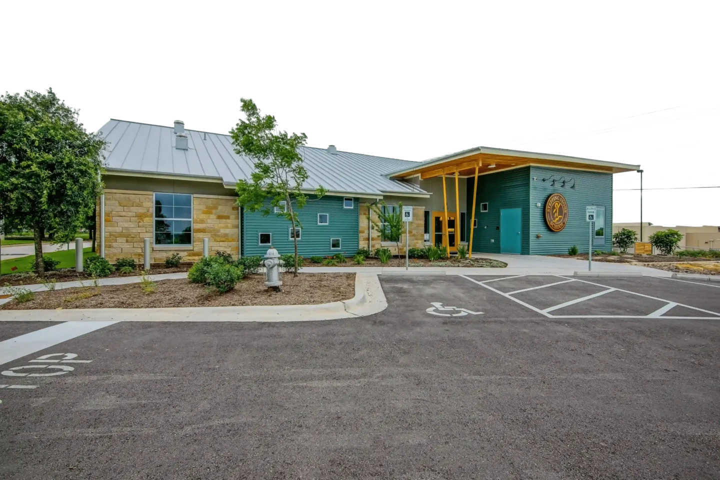 Modern building exterior with green siding and stone walls in a landscaped setting with parking spaces
