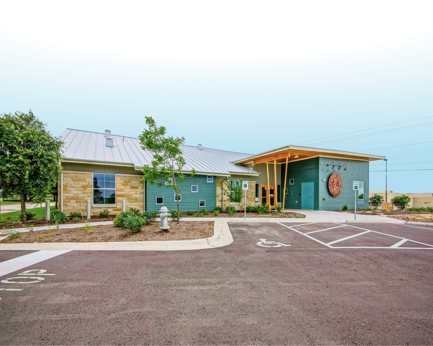 Modern building with stone and teal exterior and landscaped surroundings under a clear blue sky.