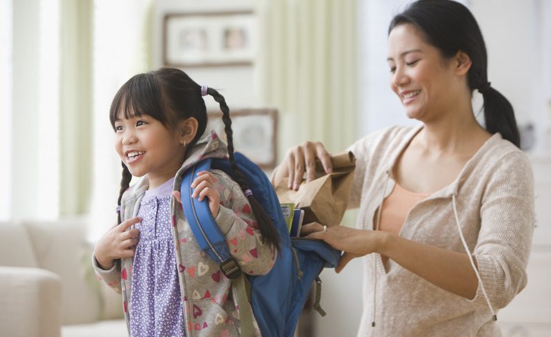 Mother packing lunch into daughter's backpack before school