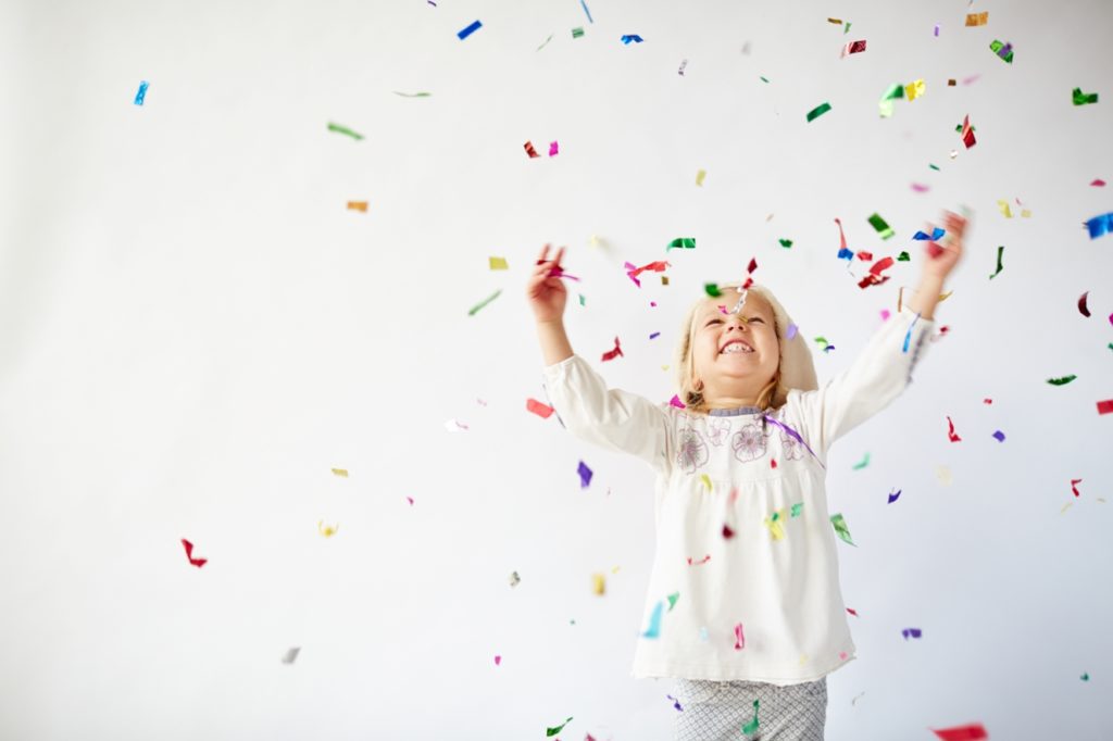 Child joyfully playing in colorful confetti against a plain background