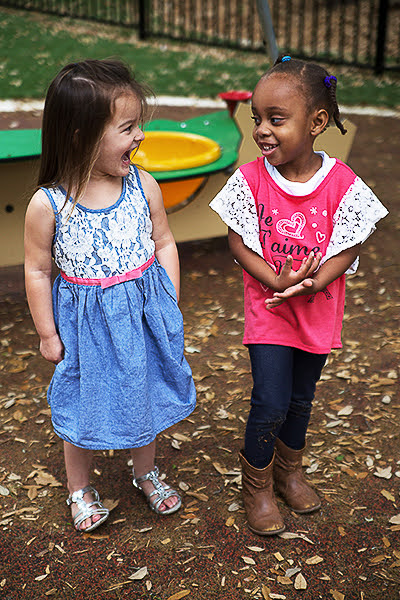 Two young girls laughing together at a playground.