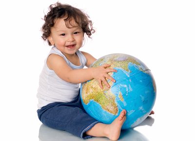 Smiling toddler sitting with a globe on a white background