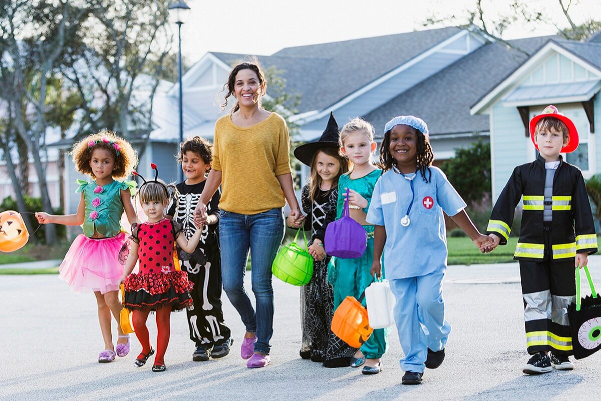Children in Halloween costumes trick-or-treating with an adult in a suburban neighborhood.