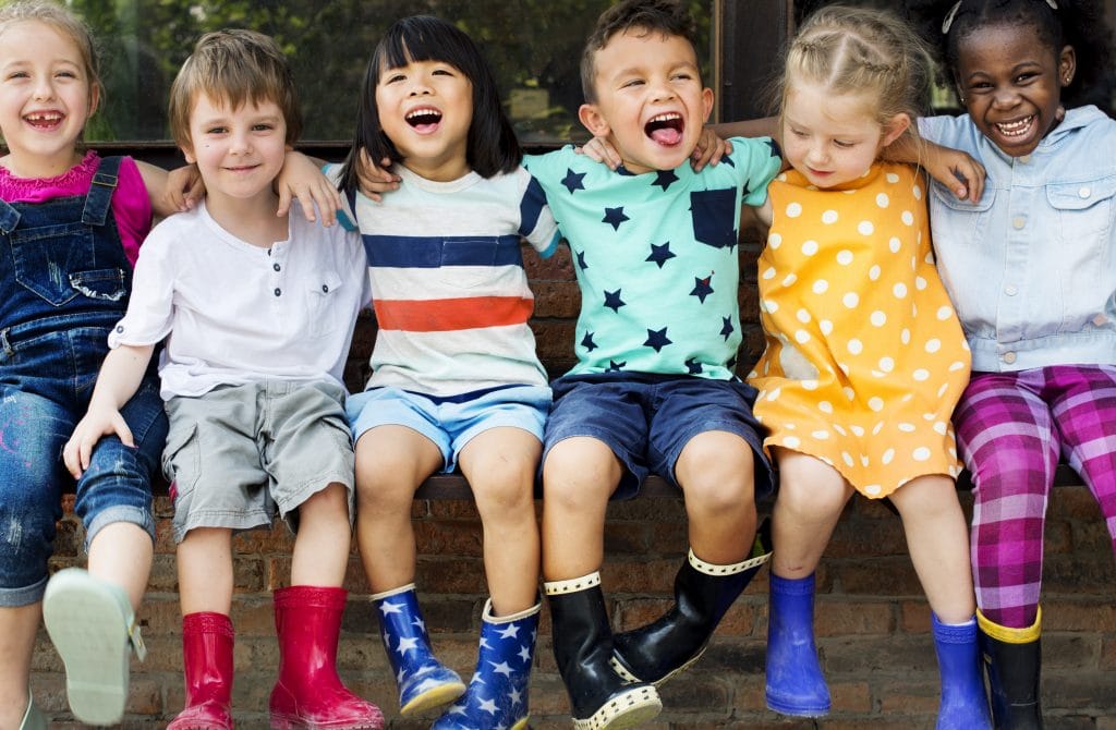 Happy children sitting together in colorful clothing and rain boots, smiling and hugging outdoors