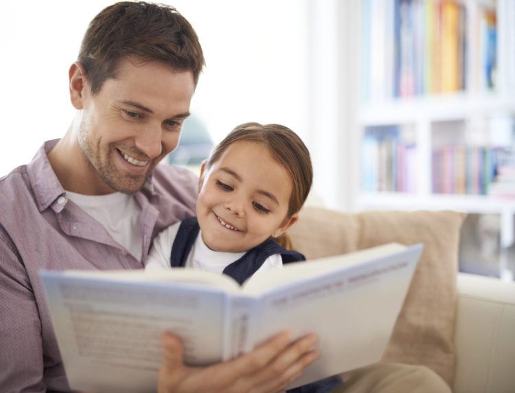 Father and daughter reading a book together on a cozy sofa at home