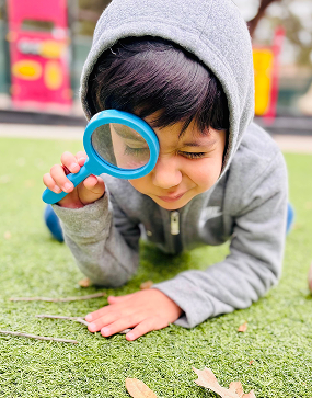 Child in hoodie uses a magnifying glass to explore grass outdoors