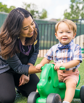 Smiling woman and toddler playing with a green toy outdoors on the grass