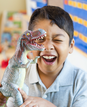 Child laughing and playing with a toy dinosaur in a classroom setting