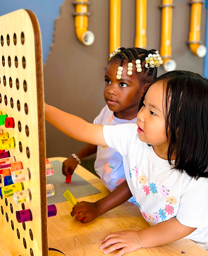 Children playing and learning with a colorful peg board in a playful indoor setting.