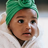 Baby wearing a green turban and cozy white outfit looking curious