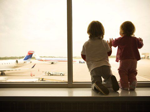 Two children watching airplanes through airport window