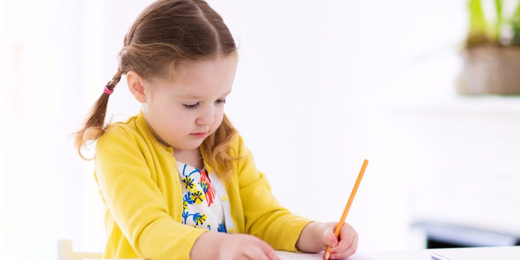 Young girl in yellow cardigan drawing with pencil at a table