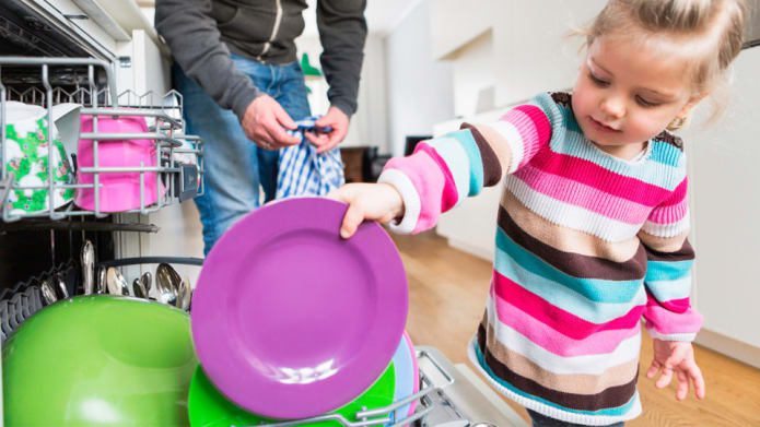 Child helping load dishwasher with colorful dishes in a home kitchen setting.