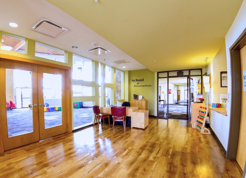 Bright school hallway with wooden floors and classroom doors School of Innovation signs visible