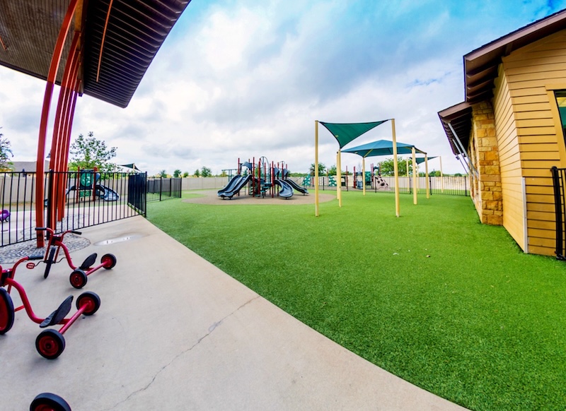 Colorful playground with slides and tricycles on artificial grass under a partly cloudy sky