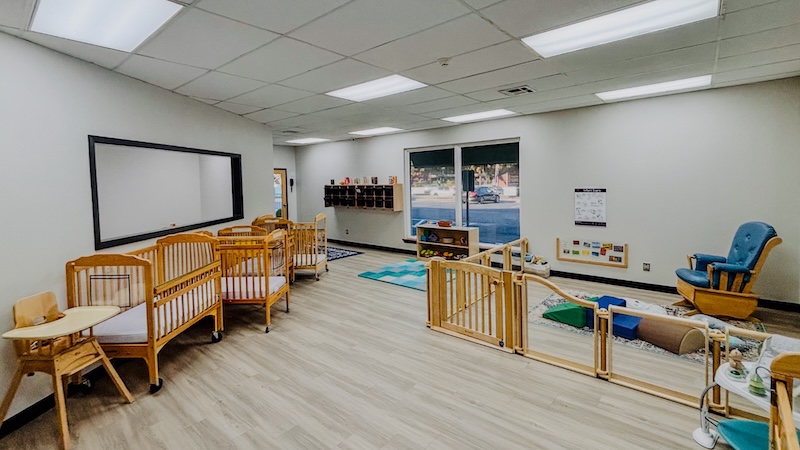 Spacious daycare room with cribs and play area for infants and toddlers