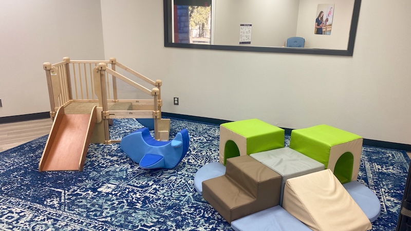 Bright indoor playroom with slide, climbing blocks, and rocking toy on a patterned blue rug