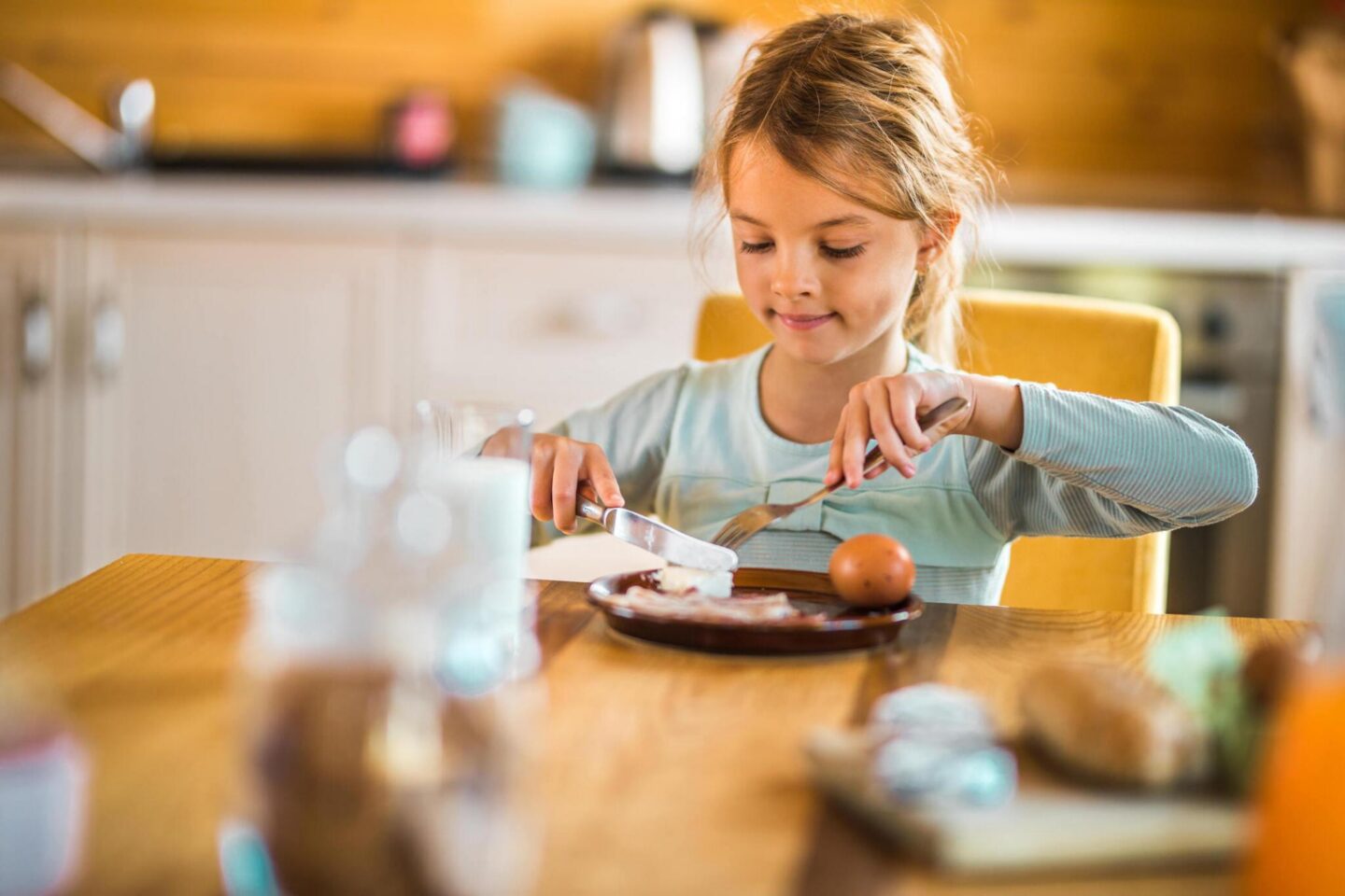 Child eating breakfast at a table with an egg and toast in a cozy kitchen setting