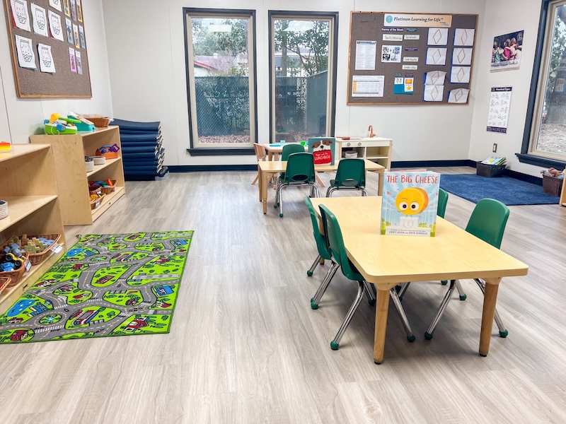 Colorful preschool classroom with tables, chairs, toys, and educational materials for young children
