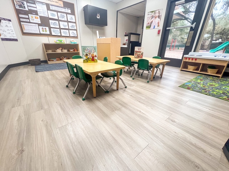 Bright classroom interior with small tables and green chairs for young children.