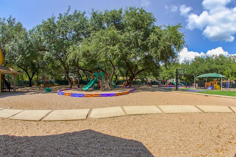 Spacious playground with a slide and trees under a clear blue sky