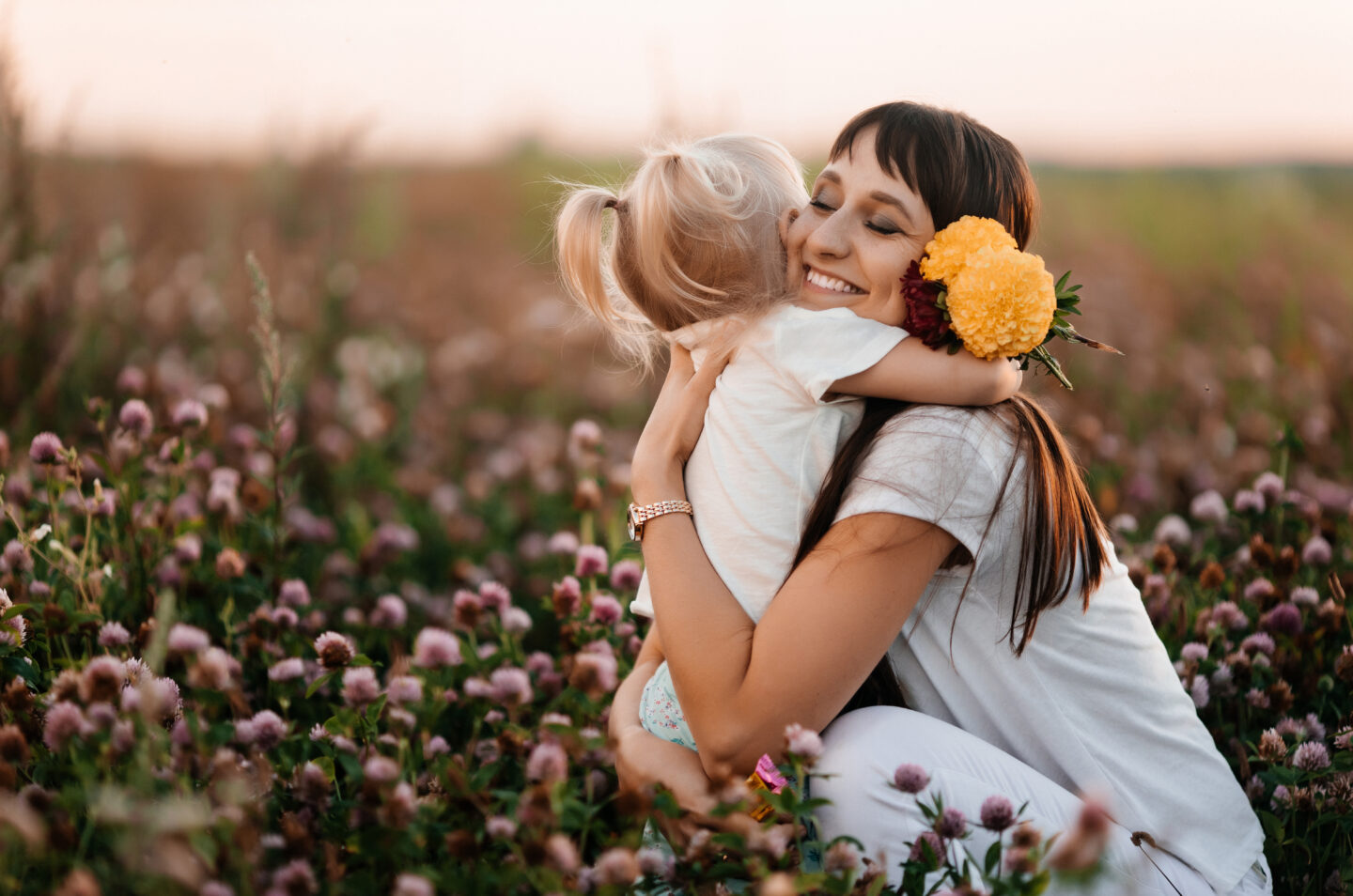 Mother and daughter embrace in a field of wildflowers at sunset