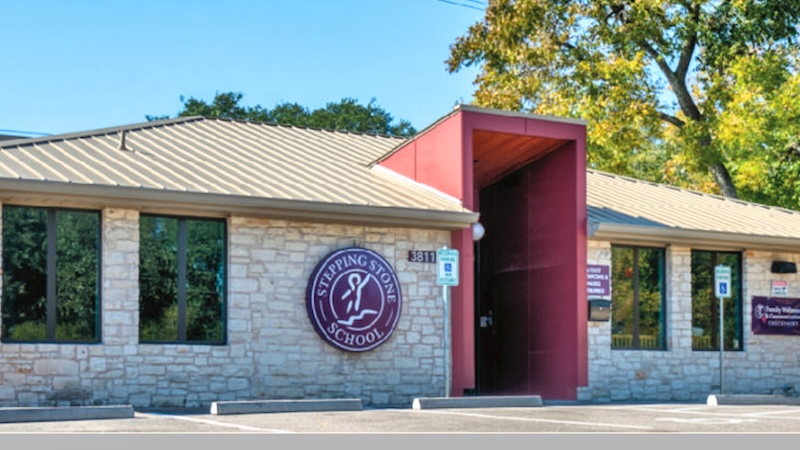 Front view of Stepping Stone School building with stone facade and red entrance under a clear sky