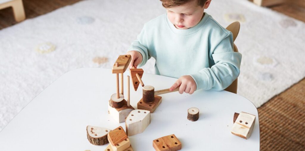 Child playing with wooden building blocks at a white table