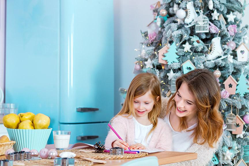 Mother and daughter decorating Christmas cookies in a festive kitchen with a tree.