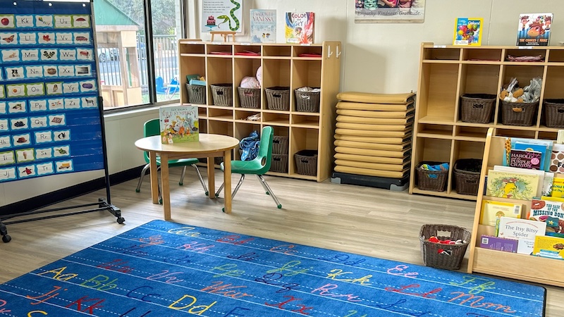 Colorful preschool classroom with alphabet rug, books, and storage shelves.