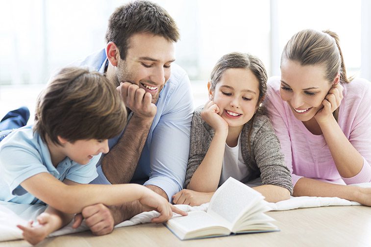 Family reading a book together on the floor and smiling