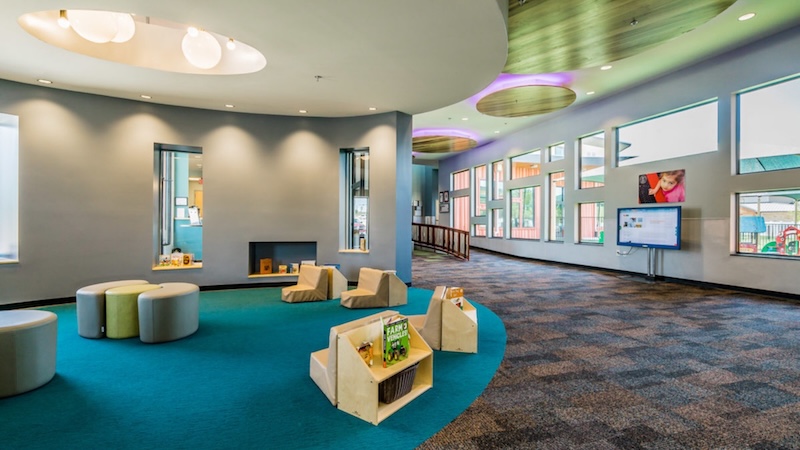 Modern school library with colorful seating and bookshelves surrounded by large windows and bright lighting