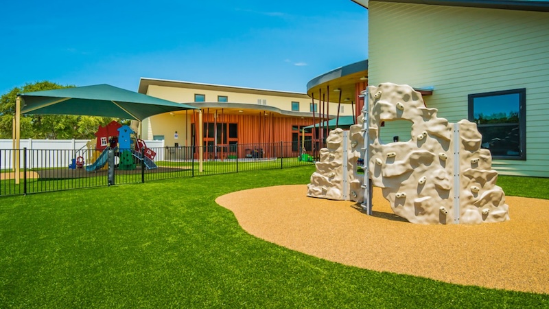 Playground with climbing wall and slide on artificial grass near modern building on a sunny day