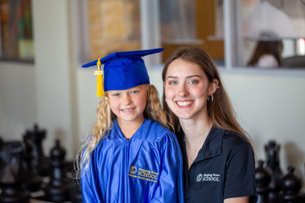 Young graduate in blue gown and cap smiles with teacher in a school setting