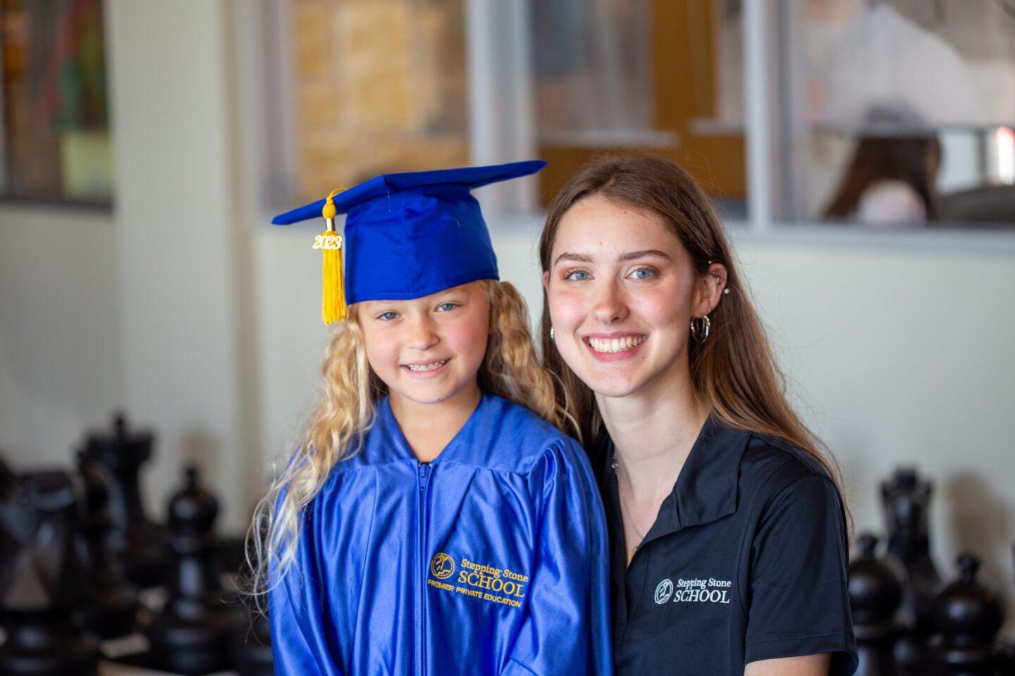Young graduate in blue gown and cap smiles with teacher in a school setting